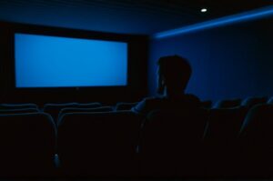 Solitary viewer sitting alone in a darkened cinema, bathed in blue light — why rewatching films is valuable for deeper understanding