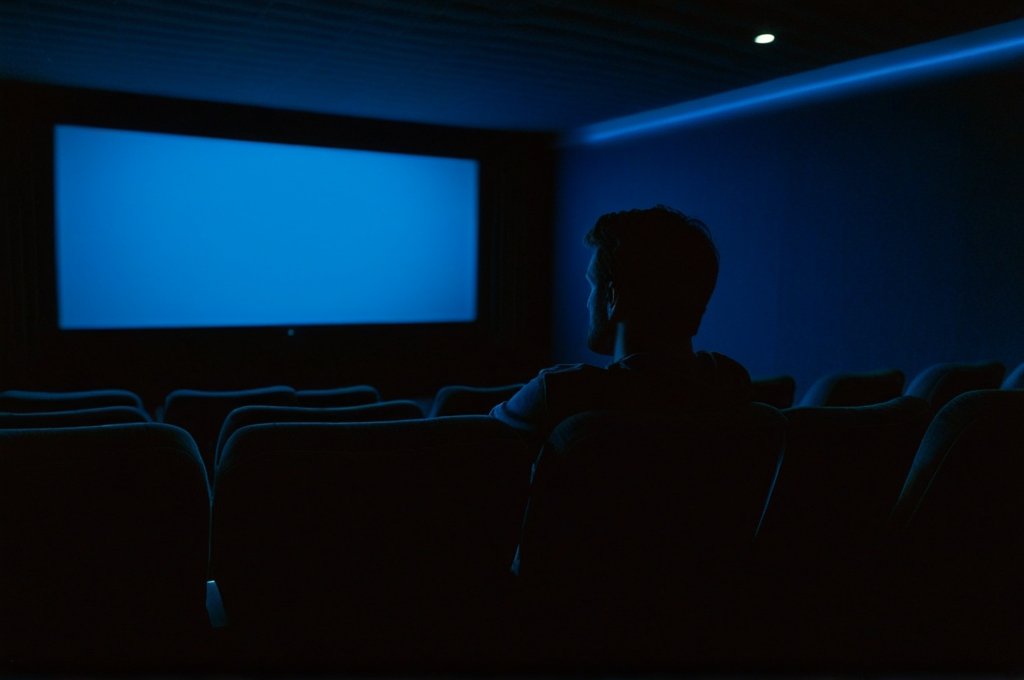 Solitary viewer sitting alone in a darkened cinema, bathed in blue light — why rewatching films is valuable for deeper understanding